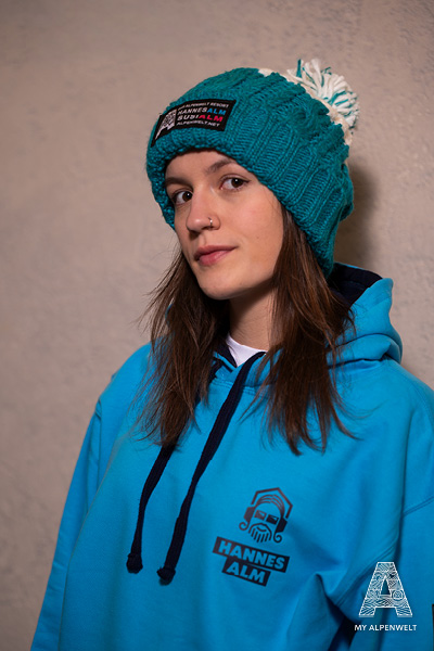 Blaue Wollmütze mit weißem Bommel und Alpenwelt-, Susi Alm und Hannes Alm Logo Patch