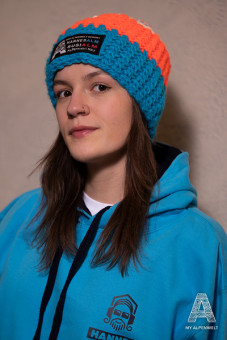 Blau-orange-weiße Wollmütze mit weißem Bommel und Alpenwelt-, Susi Alm und Hannes Alm Logo Patch